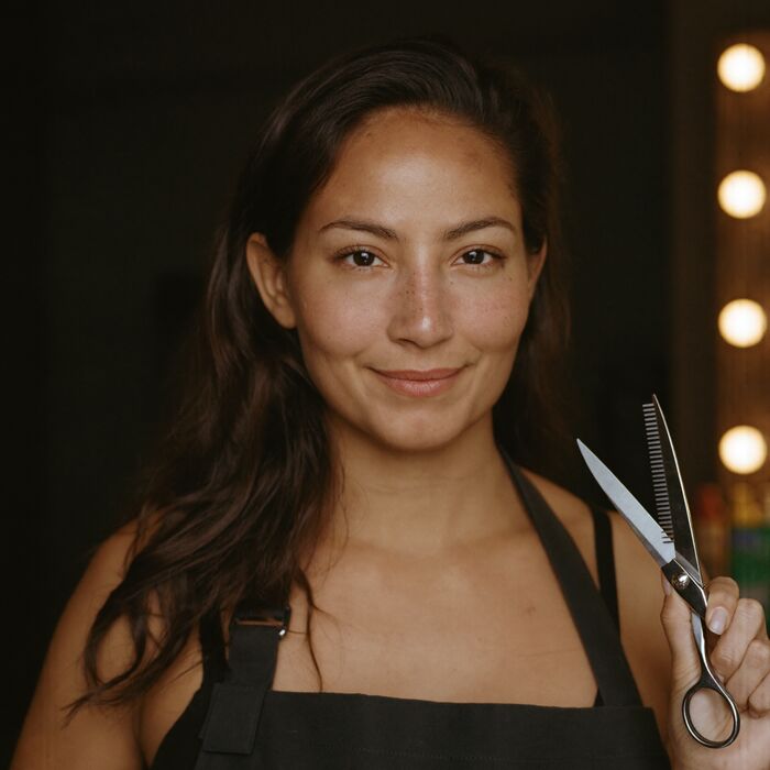A senior stylist in a black apron with shears in the pocket.