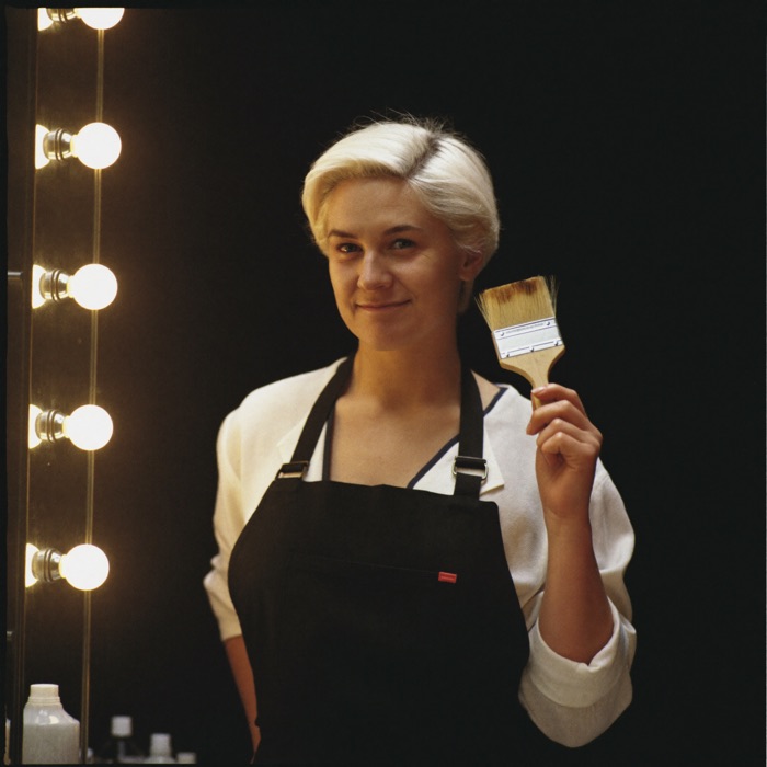 A color specialist holding a tinting brush beside a mirrored station.