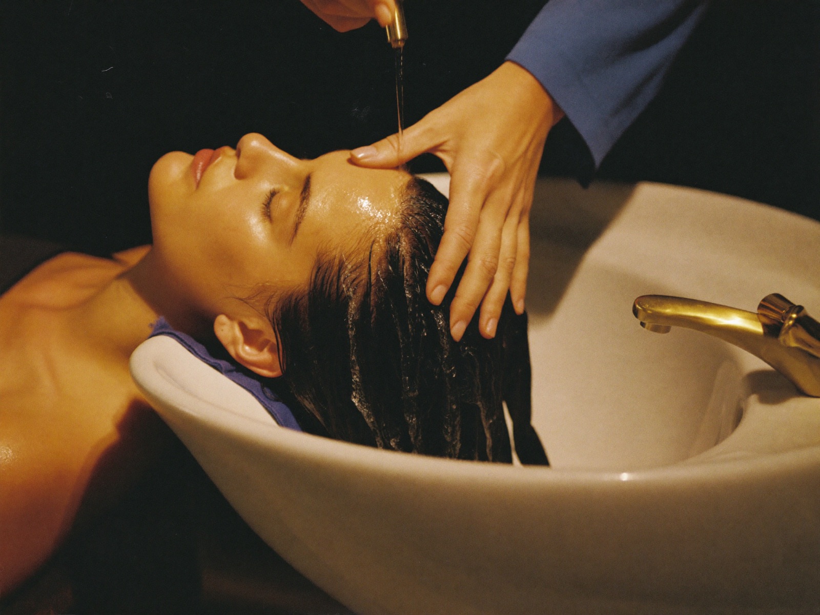 A client lying back at the shampoo basin having her hair washed.