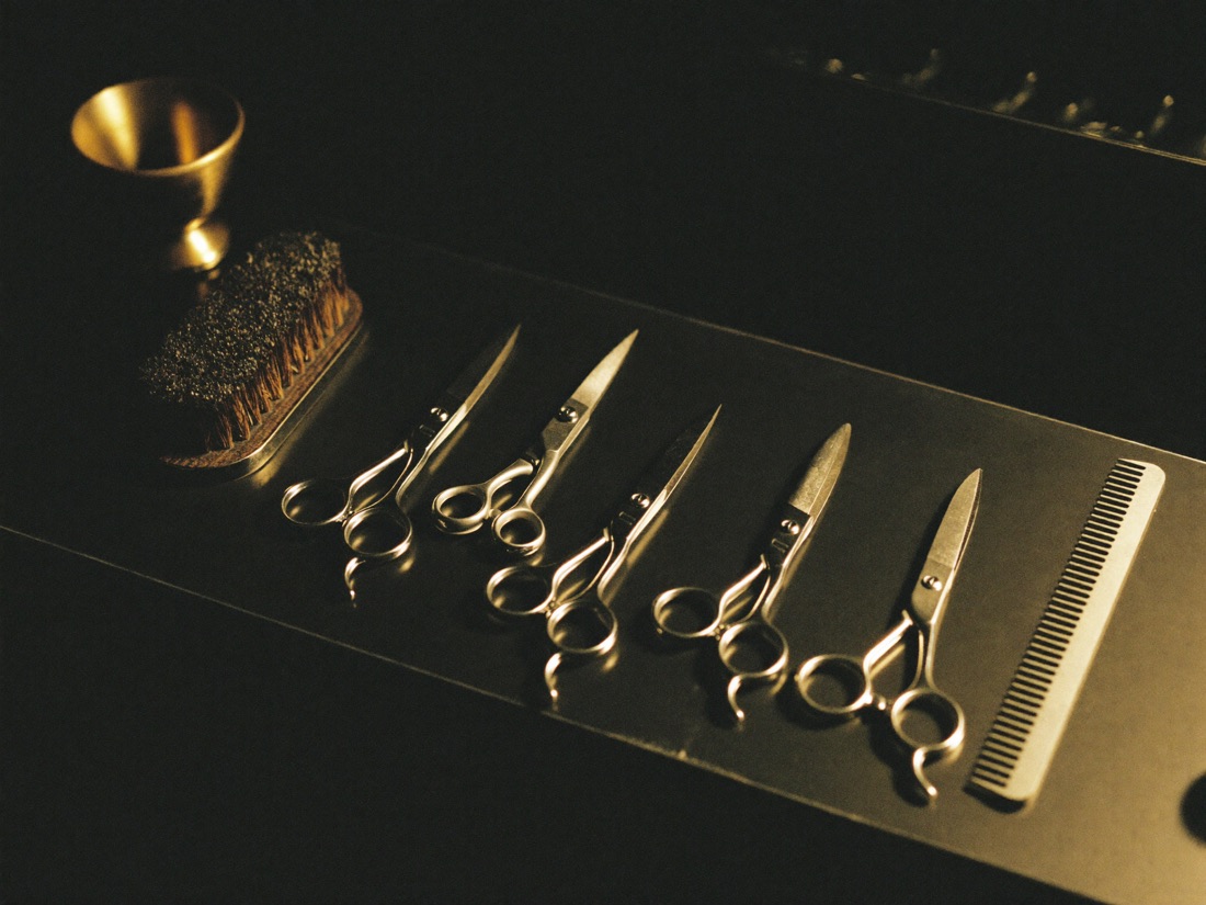 Clippers, shears, a straight razor, a neck brush and a comb laid in a row.