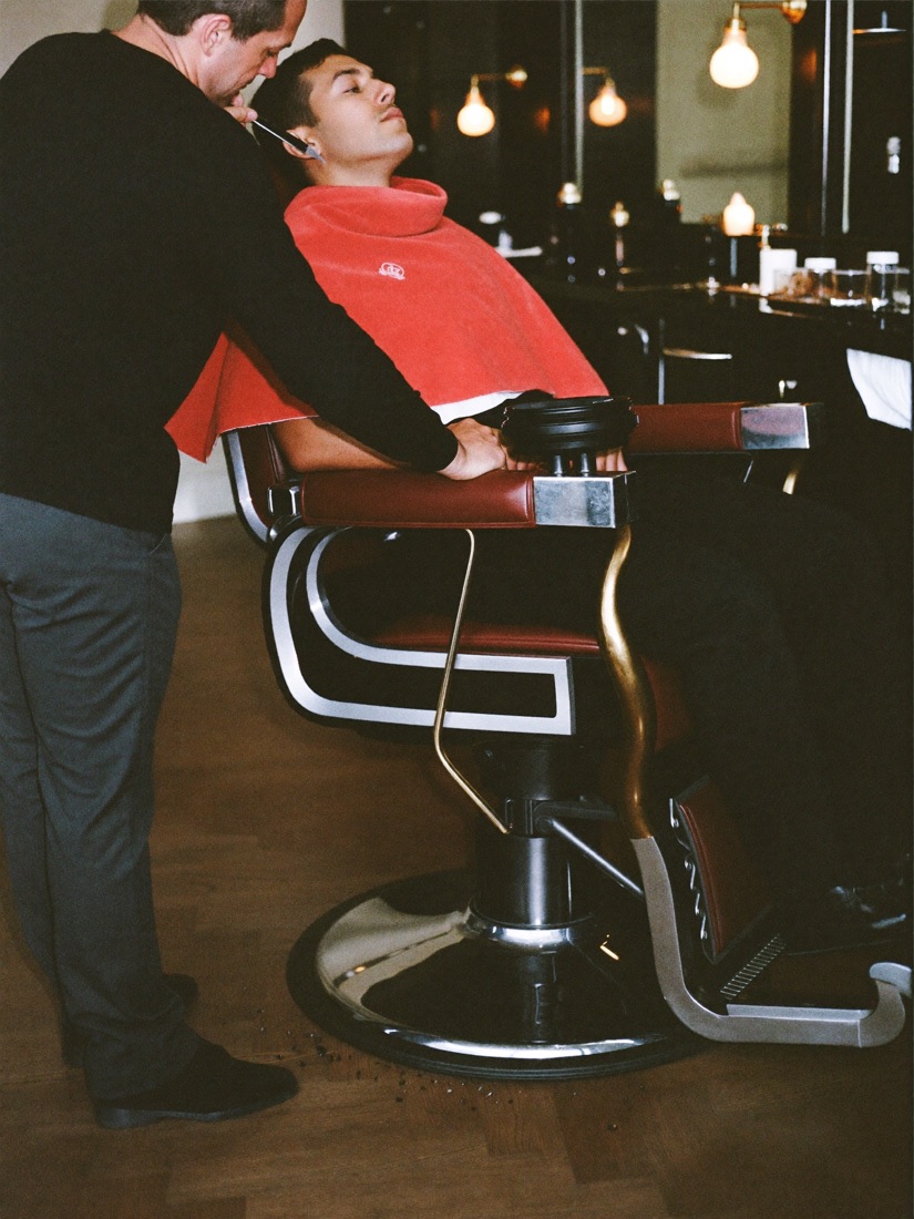 A barber working over a client reclined under a hot towel.